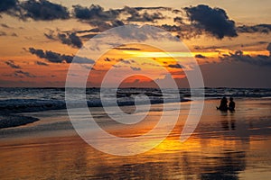 Berawa beach Pantai Berawa at sunset. Silhouettes of two people sitting in the tide. Canggu, Bali, Indonesia.