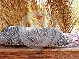 Berber chill out with fabric cushions on wood and a background of natural dry palm branches. Relaxation and Arab culture