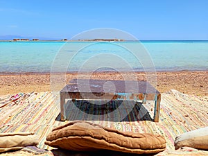 Berber chill out with rug, cushions and old table on the beach with turquoise waters of the Sinai Peninsula. Beach bars and Arab