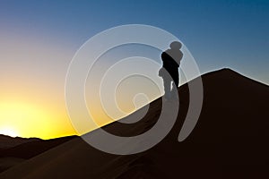 Berber man going up dunes at sunrise in Sahara, Morocco