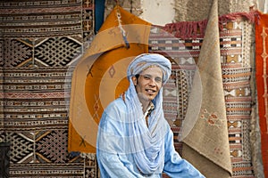 Berber man with turban in front of colorful carpets, Morocco