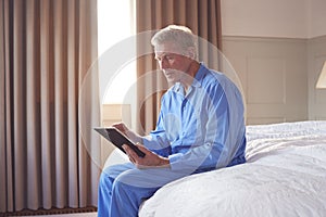 Bereaved Senior Man Sitting On Edge Of Bed Looking At Photo In Frame