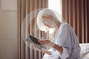 Bereaved Senior Woman Sitting On Edge Of Bed Looking At Photo In Frame photo