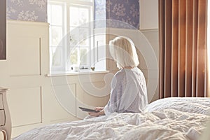 Bereaved Senior Woman Sitting On Edge Of Bed Looking At Photo In Frame photo
