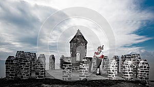 Bergamo Bagpipe. Man rings near traditional religious rural building of pebbles