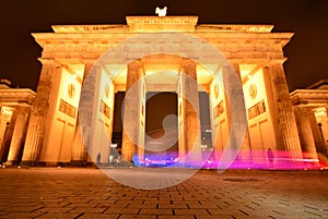 Berlin Brandenburg Gate at night time with color streak from passing vehicle showing contrast between motion vs permanence