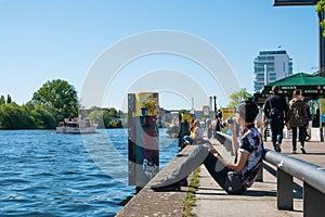 Young man drinks beer at riverside at river Spree, Berlin Wall