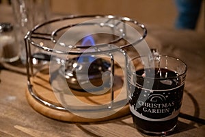Berlin / Germany - 12 13 2018: Transparent glass mug with mulled wine inside near burner for traditional French cheese fondue.