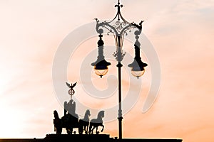 Berlin, Silhouette of Quadriga on Brandenburg Gate and nostaligic street lamp in backlight in orange evening sky at sunset photo