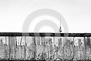 Berlin Wall original weathered section damaged with exposed iron bars partly covering the TV tower Berliner Fernsehturm