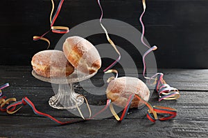 Berliner doughnuts or Krapfen with colorful party streamers on a dark rustic wooden table, traditional pastry for New Year or