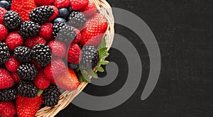 Berries in a basket closeup. Fresh ripe raspberries, blackberries, strawberries and blueberries on black background. Berry mix.