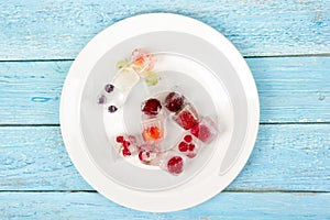 Berries frozen in ice cubes with mint on plate.
