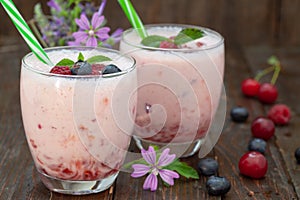 Berries smoothies in two glasses with straws on wooden table