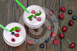 Berries smoothies in two glasses with straws on wooden table