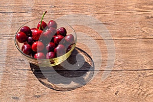 Berries of a sweet cherry in a glass bowl on a wooden background. Ripe red sweet cherry