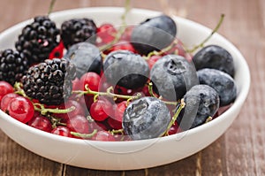 berries in a white bowl/ abundance of berries in a white bowl on a wooden background. Selective focus