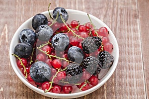 Berries in a white bowl/ abundance of berries in a white bowl on a wooden background. Top view