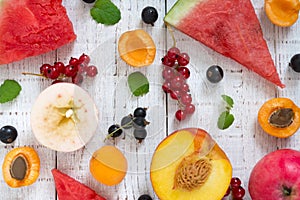 Berry background. Many summer fruits and berries are scattered on a white wooden background.