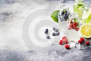 Berry and citrus soft drinks and cocktails in glass bottles on gray stone table background, copy space