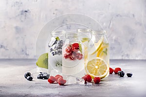 Berry and citrus soft drinks and cocktails in glass bottles on gray stone table background, copy space