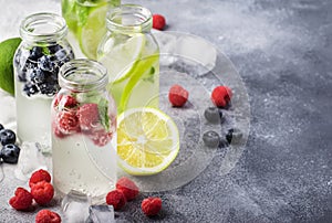 Berry and citrus soft drinks and cocktails in glass bottles on gray stone table background, copy space