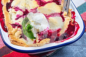 Berry cobbler in enamel baking dish, garnished with ice cream, horizontal, closeup