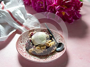 Berry crumble with ice cream on plate. Pink background with lilac peonies. Copy space. Closse up
