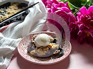 Berry crumble with ice cream on plate. Pink background with lilac peonies. Copy space. Closse up