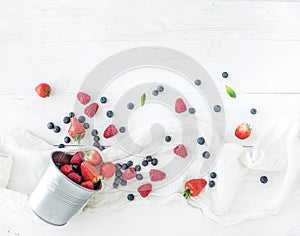 Berry frame with copy space on right. Metal bucket, strawberries, raspberries, blueberries and mint leaves, white wooden