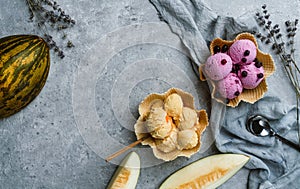 Berry and melon ice cream scoops on waffle basket on light grey background with flowers and fresh melon. Summer ice cream dessert