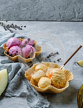 Berry and melon ice cream scoops on waffle basket on light grey background with flowers and fresh melon. Summer ice cream dessert