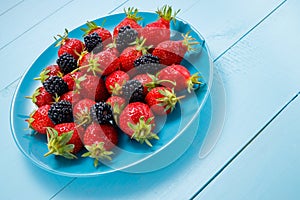 Berry mix with strawberry and raspberry on a plate and wooden table, antioxidant organic superfood concept for healthy eating and