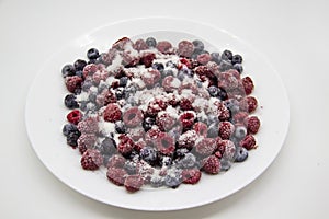 A Berry mix in sugar from frozen raspberries and blueberries on the white plate. A Frozen Berries with Sugar.  A sweet background