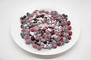 A Berry mix in sugar from frozen raspberries and blueberries on the white plate. A Frozen Berries with Sugar.  A sweet background