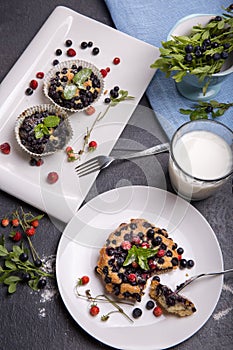 Berry muffin with blueberries and strawberries on a white plate and a wooden table served with milk and and fresh