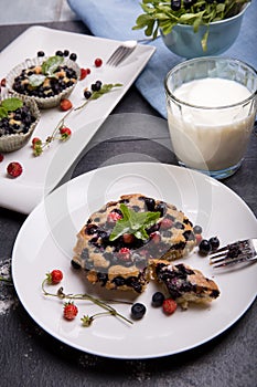 Berry muffin with blueberries and strawberries on a white plate and a wooden table served with milk and and fresh