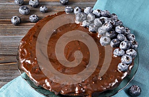 Berry pie ,1 round chocolate homemade cake with fresh blueberries on a blue towel and wooden brown background