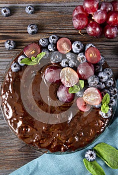 Berry pie on  blue towel,  round chocolate homemade cake with fresh blueberries and red grapes, mint on a wooden brown background