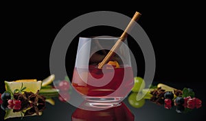 Berry still life with a drink on a black background and cinnamon in a glass.