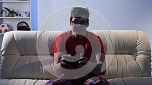 Bespectacled man playing video game while sitting on the couch