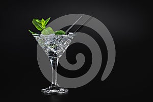 The best cocktail in a martini glass with ice and mint on a black background, top view, black cocktail tube.