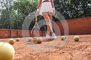 She is the best! Cropped image of sexy female tennis player on outdoor court. Sporty young woman with tennis racket and several