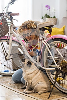 Best friend forever little adorable pug dog at home with her female cheerful owner repairing a coloured happy bike - concept of