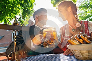 Best friends in Bavarian Tracht sitting in Beer garden or oktoberfest and enjoying a glass of beer and the sun