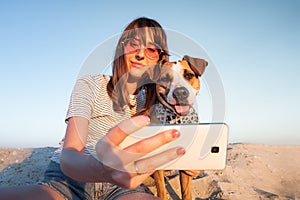 Best friends concept: human taking a selfie with dog. Young female makes self portrait with her puppy outdoors on a beach