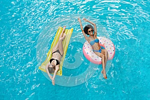 Best friends on donut ring and lilo floating in pool together, overhead view
