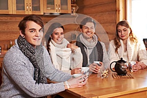 Best friends drinking hot tea in cosy kitchen at winter cottage