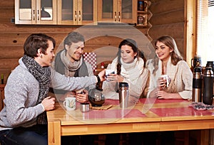 Best friends drinking hot tea in cosy kitchen at winter cottage