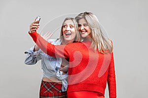 Best friends having fun. Portrait of happy women in stylish clothes taking selfie, isolated on gray background